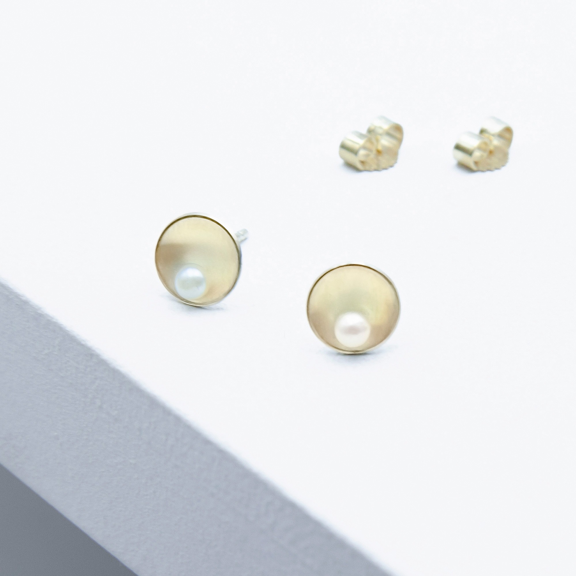 Ohrringe aus 585er Gelbgold mit 8-mm gewölbten Plättchen, mattierter Oberfläche, polierten Kanten und je einer weißen 3-mm Akoya-Perle.